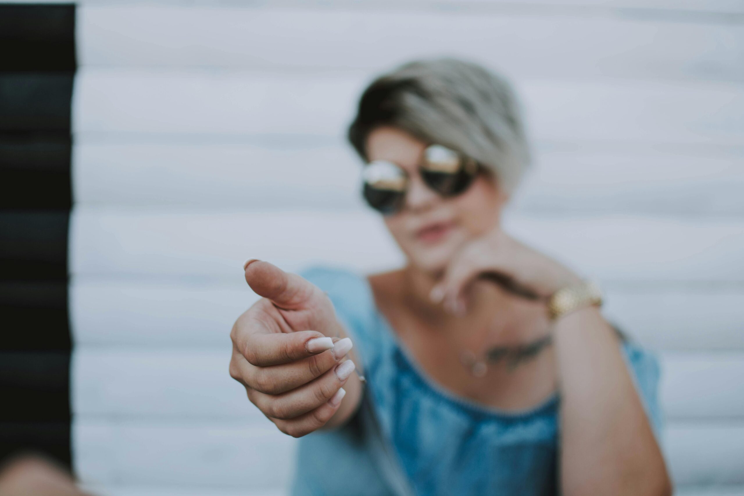 Fashionable woman wearing sunglasses extends hand, inviting gesture.